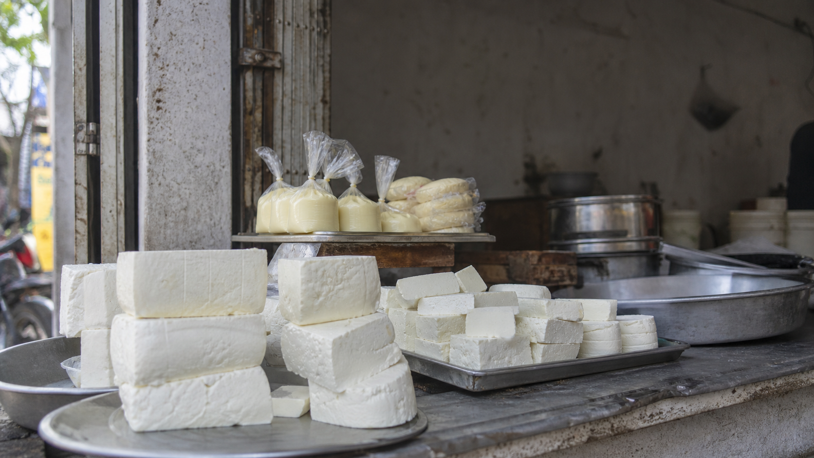 Blocks of fresh paneer on display at a market stall with a vendor arranging dairy products on a wooden counter.
