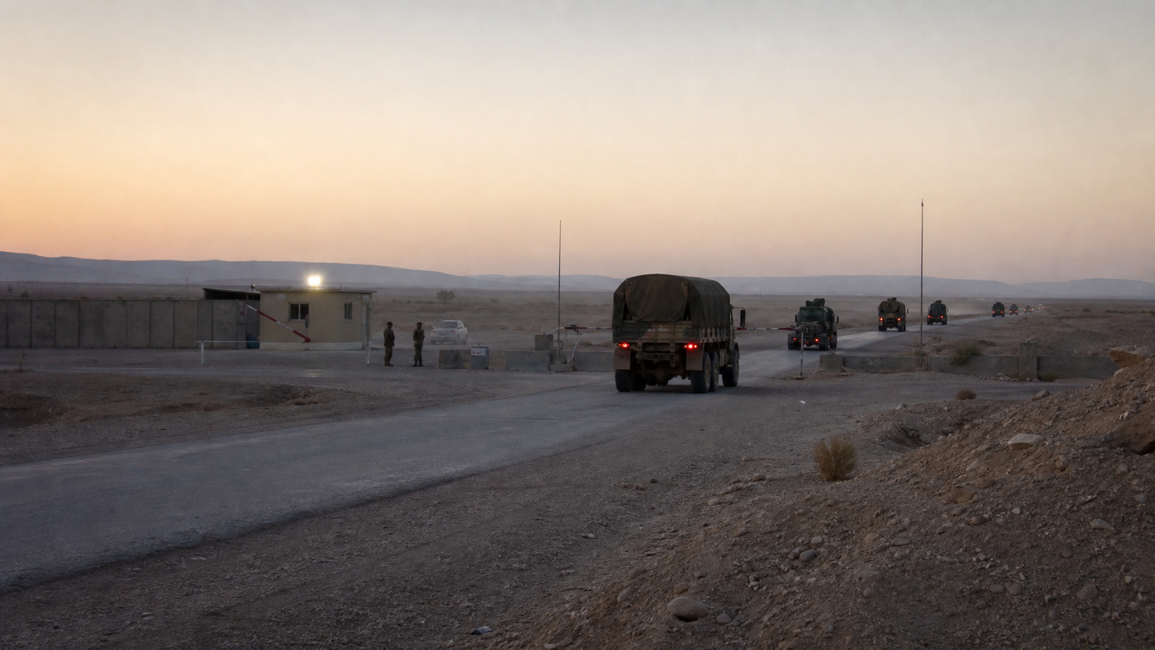 US military convoy leaving a desert base perimeter at dusk in Iraq, with Iraqi security personnel at a roadside checkpoint and heat haze over the road