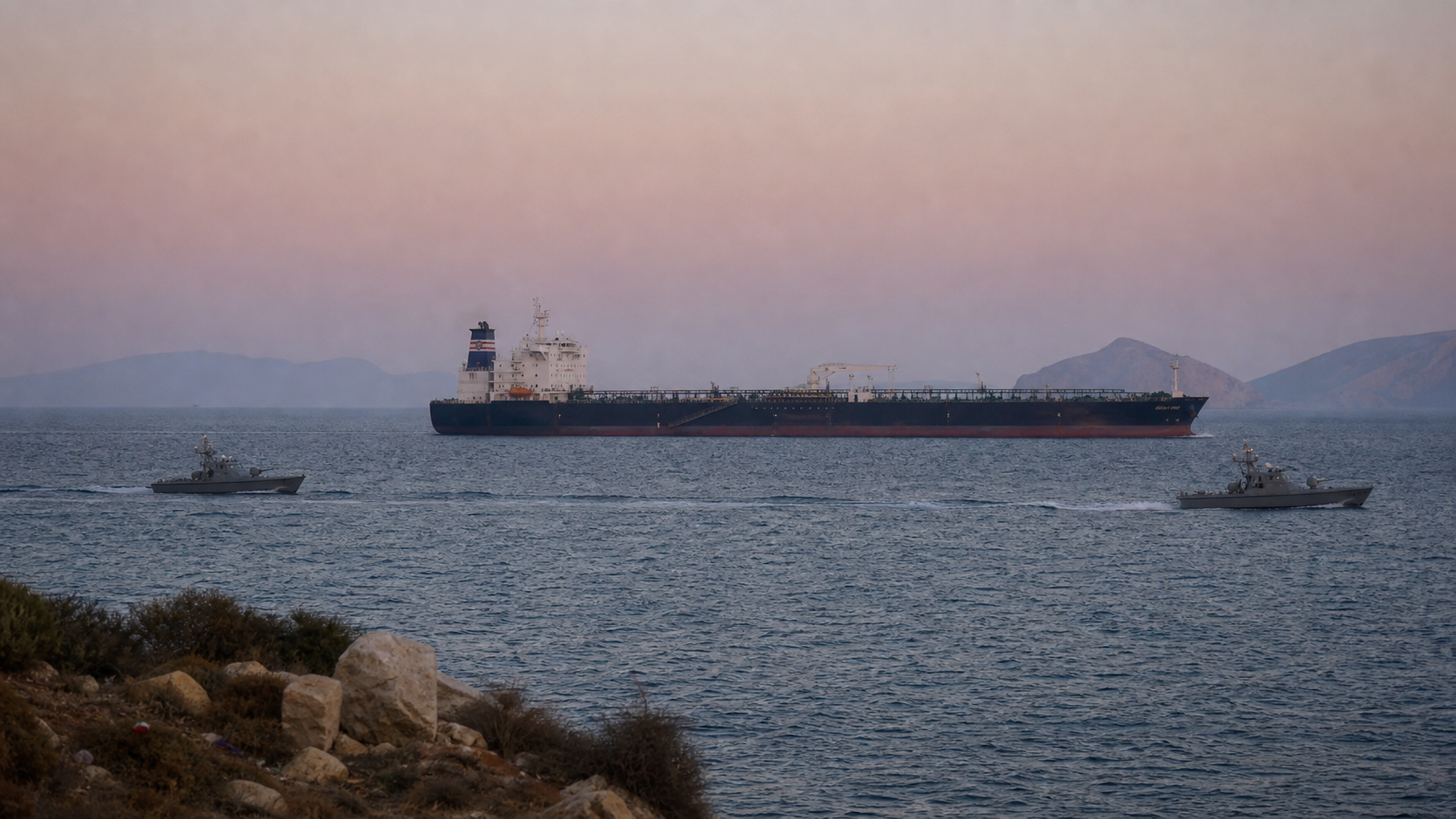 A wide, dusk-lit view shows tanker traffic moving through hazy waters near the Strait of Hormuz as two small patrol craft pass in the distance, underscoring tense but open-ended maritime conditions.
