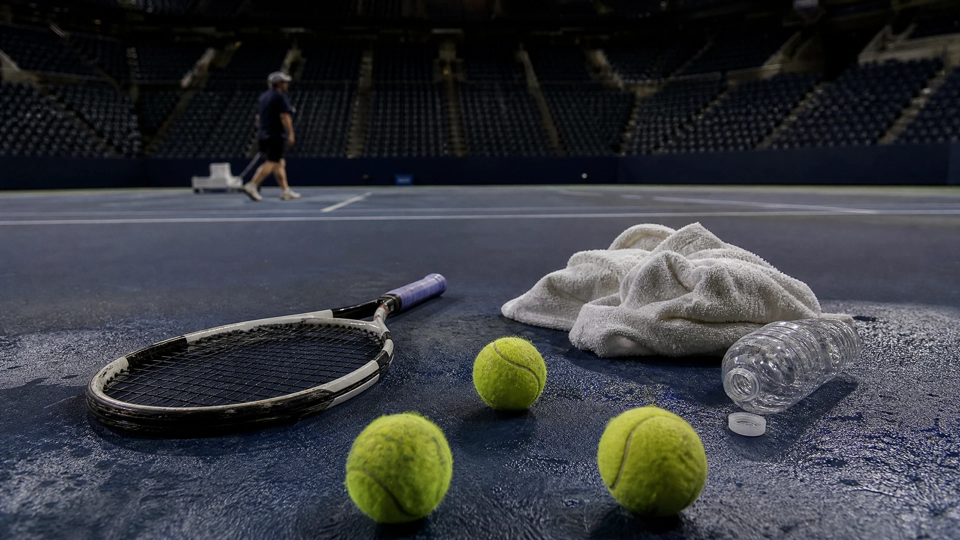 A scuffed racket, used balls and a crumpled towel lie on a blue hardcourt after a night match.
