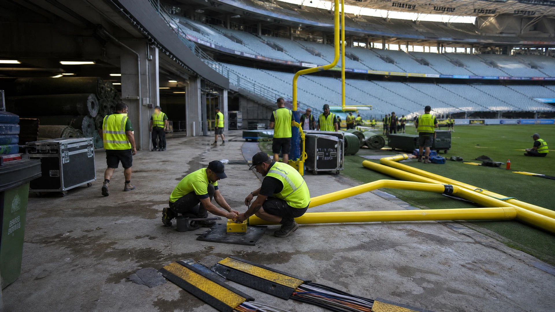 Workers assemble temporary American-football equipment inside an empty Australian stadium.