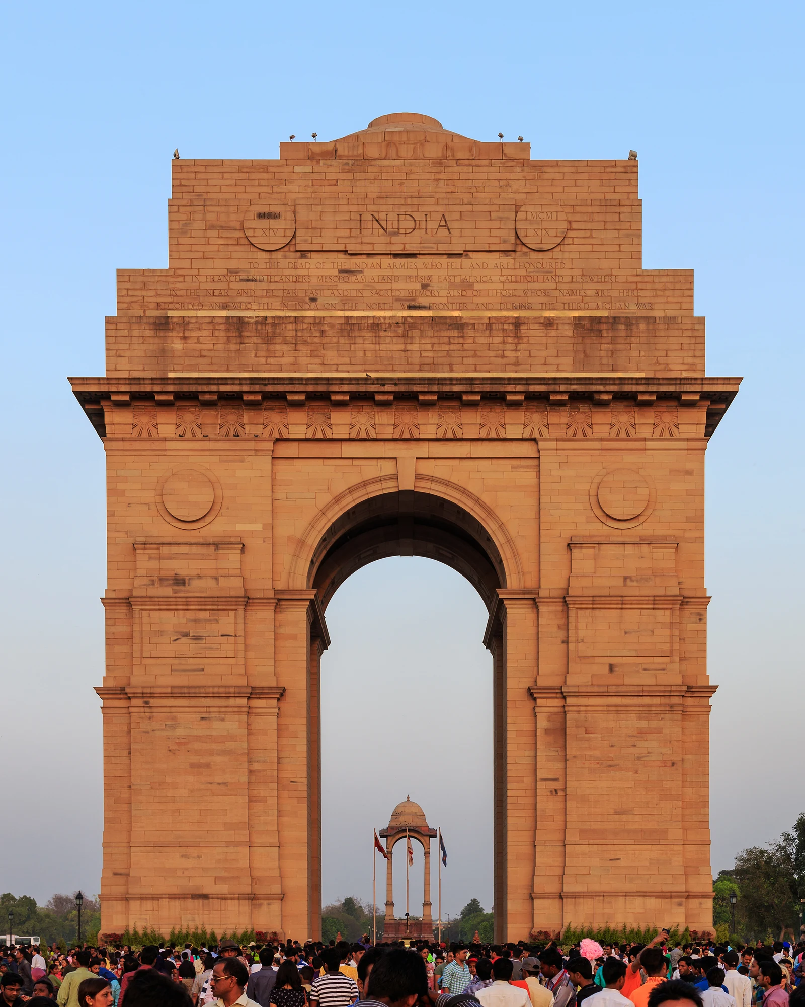India Gate monument in New Delhi viewed from the front under a blue sky, with visitors at its base